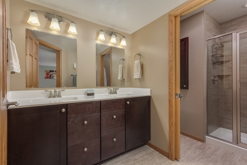 Mid-sized transitional master bathroom in Minneapolis with flat-panel cabinets, dark wood cabinets, an alcove shower, a two-piece toilet, beige tile, porcelain tile, brown walls, porcelain floors, an integrated sink, engineered quartz benchtops, beige floor, a hinged shower door and white benchtops.