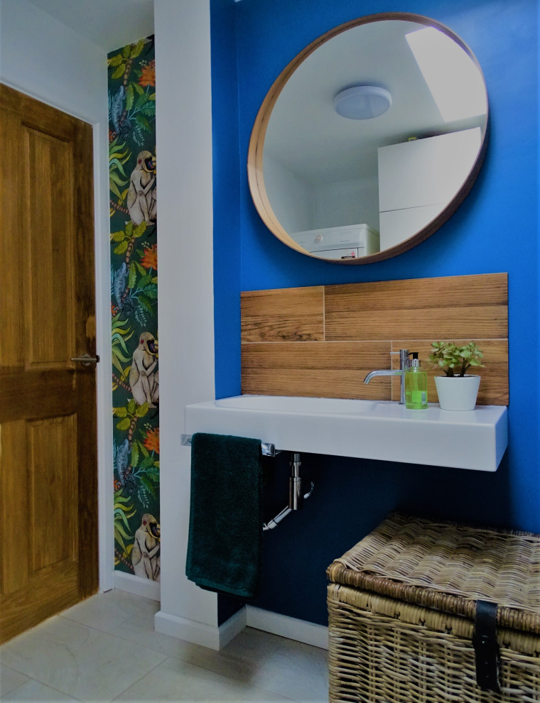 This is an example of a small eclectic powder room in Gloucestershire with brown tile, wood-look tile, blue walls, ceramic floors, a wall-mount sink, beige floor, a floating vanity and wallpaper.