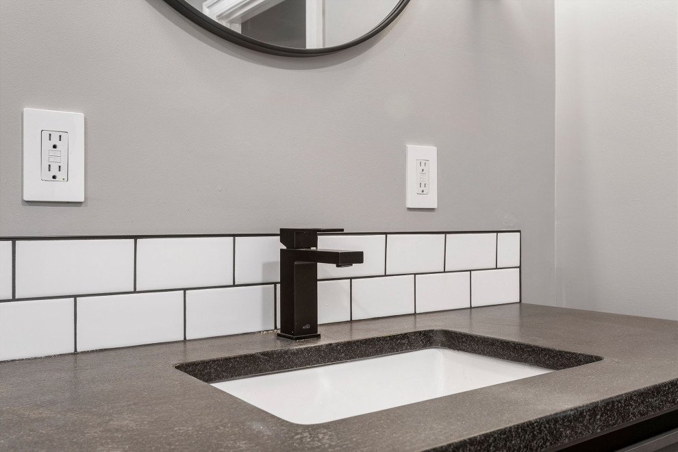 Cette image montre une grande salle de bain principale minimaliste avec un carrelage blanc, un carrelage métro, un sol en carrelage de porcelaine, un plan de toilette en quartz modifié, un sol gris, une cabine de douche à porte battante, un plan de toilette noir, buanderie et meuble simple vasque.