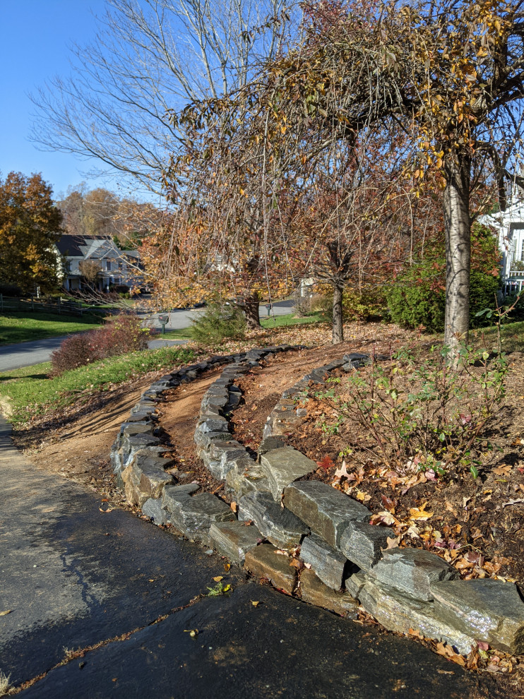 Photo of a large traditional front yard full sun driveway in Other with a retaining wall, natural stone pavers and a wood fence.