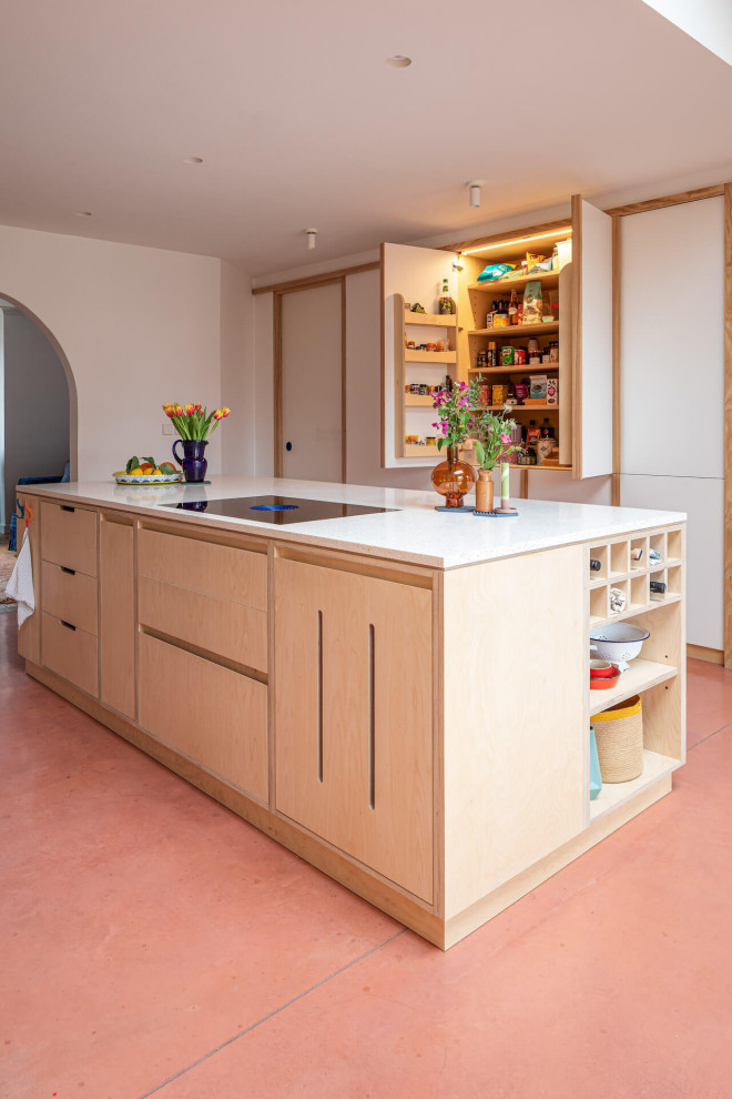Cette image montre une grande cuisine ouverte parallèle design en bois clair avec un placard à porte plane, sol en béton ciré, îlot et un sol rose.