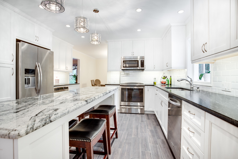 Design ideas for a large transitional u-shaped kitchen in DC Metro with an undermount sink, recessed-panel cabinets, white cabinets, granite benchtops, white splashback, subway tile splashback, stainless steel appliances and with island.