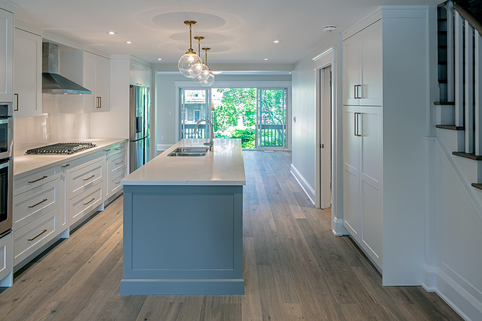 Inspiration for a mid-sized transitional galley open plan kitchen in Toronto with an undermount sink, shaker cabinets, grey cabinets, quartz benchtops, white splashback, subway tile splashback, stainless steel appliances, light hardwood floors, with island, beige floor and white benchtop.