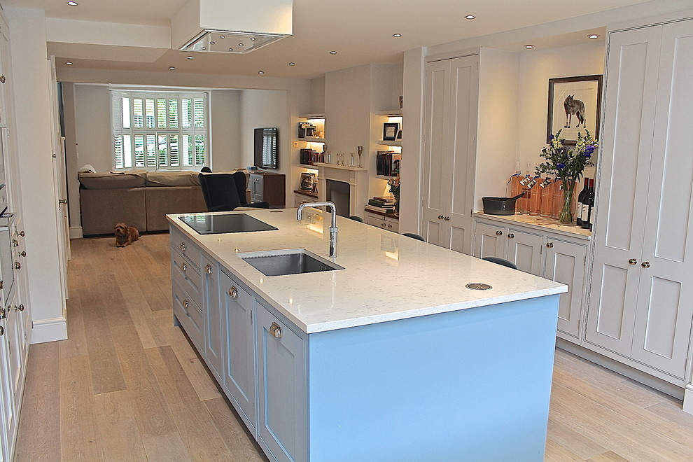 Photo of a mid-sized transitional open plan kitchen in London with a drop-in sink, shaker cabinets, white cabinets, quartzite benchtops, stainless steel appliances, light hardwood floors and with island.