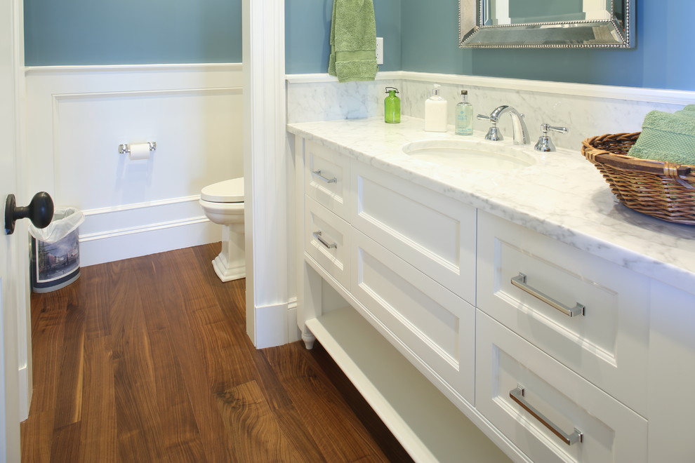 This is an example of a large beach style bathroom in Boston with beaded inset cabinets, white cabinets, blue walls, dark hardwood floors, an undermount sink, marble benchtops and brown floor.