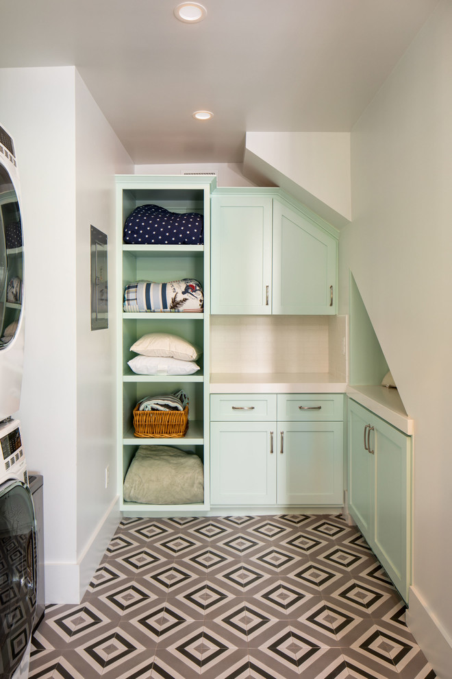 Design ideas for a beach style u-shaped dedicated laundry room in Los Angeles with shaker cabinets, green cabinets, white walls, a stacked washer and dryer, multi-coloured floor and white benchtop.