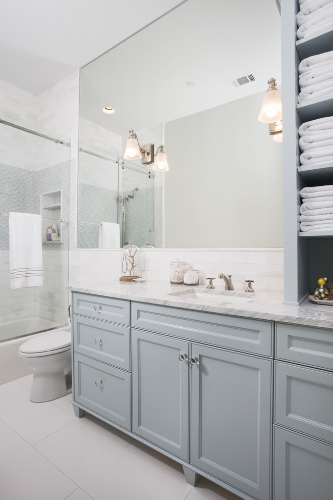 This is an example of a mid-sized transitional kids bathroom in Austin with recessed-panel cabinets, grey cabinets, a shower/bathtub combo, white tile, ceramic tile, white walls, terra-cotta floors, an undermount sink, marble benchtops and grey floor.