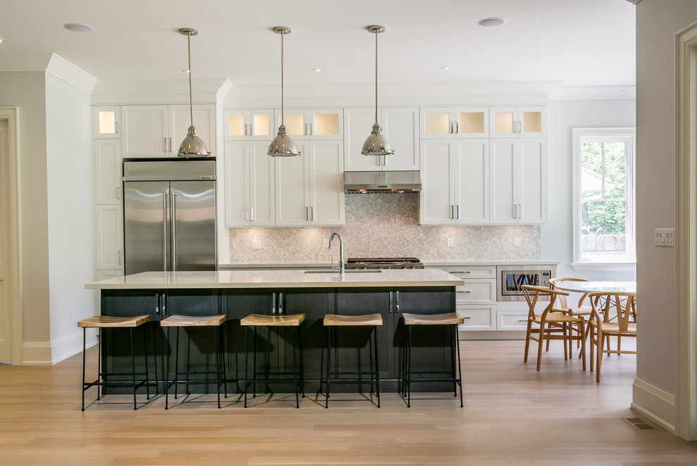 This is an example of a large transitional single-wall eat-in kitchen in Toronto with shaker cabinets, white cabinets, quartzite benchtops, grey splashback, with island, stainless steel appliances, an undermount sink, mosaic tile splashback and light hardwood floors.