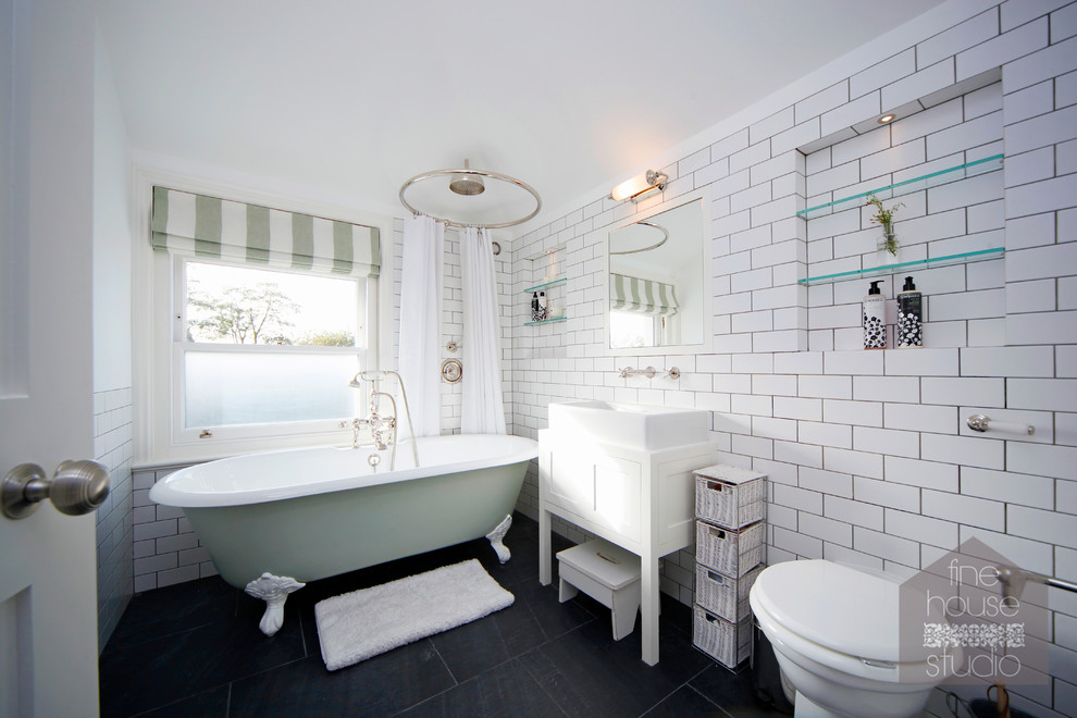 Inspiration for a mid-sized eclectic master bathroom in Gloucestershire with a console sink, furniture-like cabinets, white cabinets, a freestanding tub, a one-piece toilet, white tile, ceramic tile, white walls and slate floors.