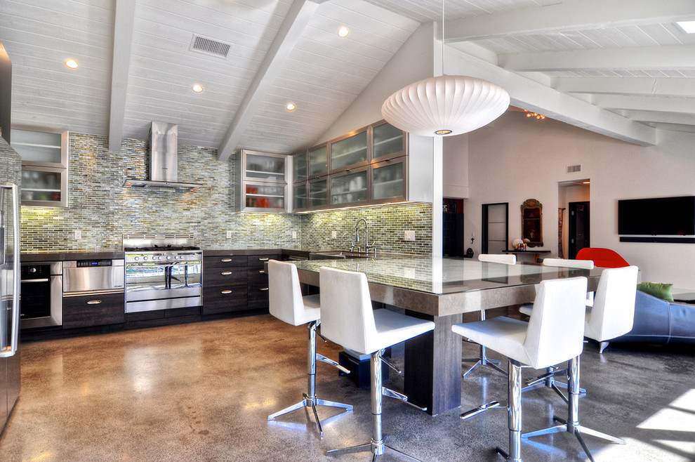 Midcentury u-shaped eat-in kitchen in Orange County with a farmhouse sink, quartz benchtops, blue splashback, glass tile splashback, stainless steel appliances, glass-front cabinets, brown cabinets, concrete floors and with island.