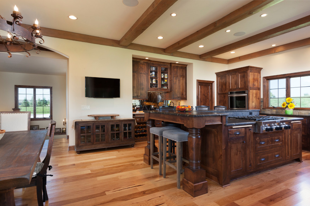 This is an example of a large traditional l-shaped eat-in kitchen in Milwaukee with an undermount sink, flat-panel cabinets, medium wood cabinets, granite benchtops, brown splashback, ceramic splashback, stainless steel appliances, light hardwood floors, with island and black benchtop.