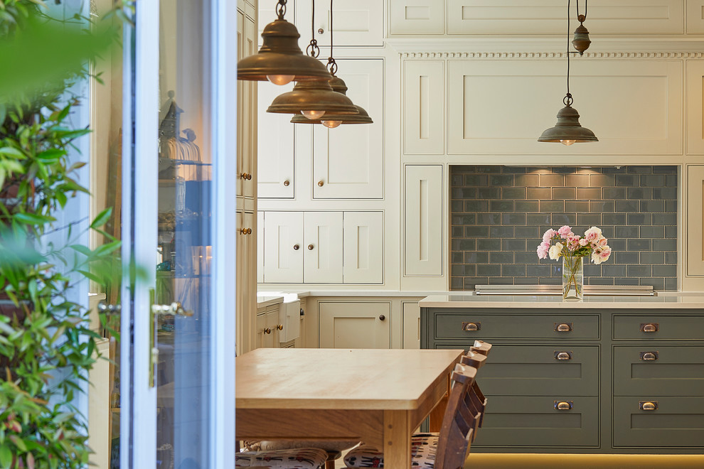Large traditional l-shaped eat-in kitchen in Surrey with a farmhouse sink, shaker cabinets, beige cabinets, solid surface benchtops, grey splashback, porcelain splashback, black appliances, porcelain floors, with island, beige floor and white benchtop.