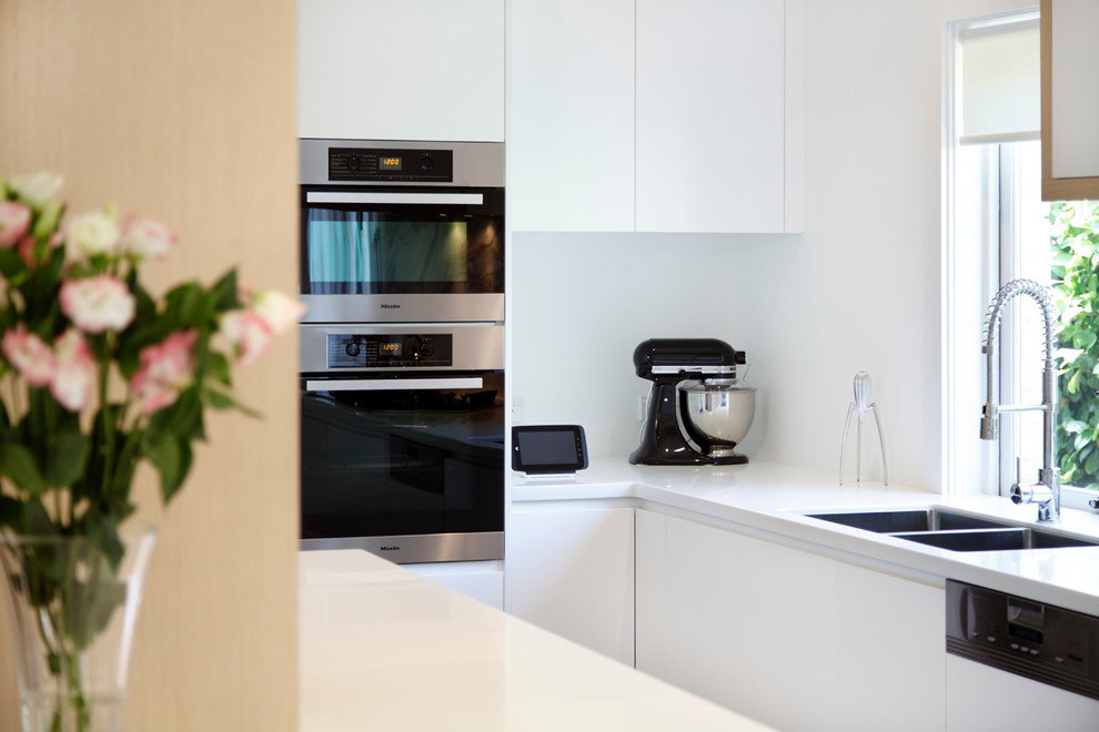 Design ideas for a modern single-wall eat-in kitchen in Sydney with a drop-in sink, flat-panel cabinets, white cabinets, solid surface benchtops, stone slab splashback and stainless steel appliances.