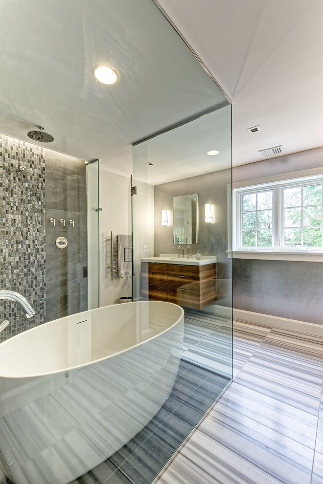 Freestanding bathtub - mid-sized transitional master gray tile and porcelain tile marble floor and gray floor freestanding bathtub idea in New York with furniture-like cabinets, medium tone wood cabinets, a wall-mount toilet, gray walls, an undermount sink, quartz countertops, a hinged shower door and white countertops