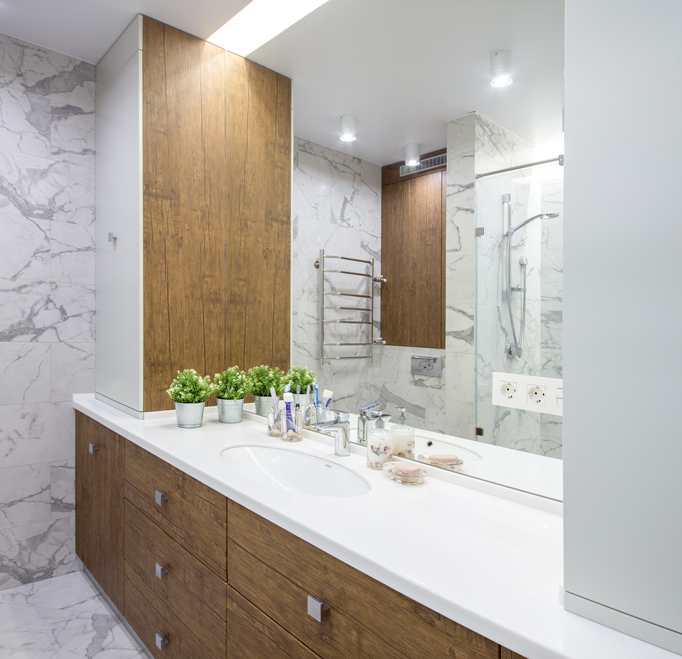 Photo of a mid-sized contemporary 3/4 bathroom in Novosibirsk with flat-panel cabinets, medium wood cabinets, an alcove shower, a wall-mount toilet, white tile, porcelain tile, white walls, porcelain floors, an undermount sink, solid surface benchtops, white floor, a hinged shower door and white benchtops.
