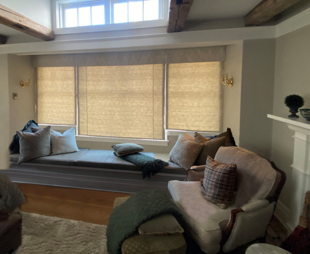 Inspiration for a transitional master bedroom in Burlington with beige walls, medium hardwood floors, a standard fireplace, a wood fireplace surround, beige floor and exposed beam.