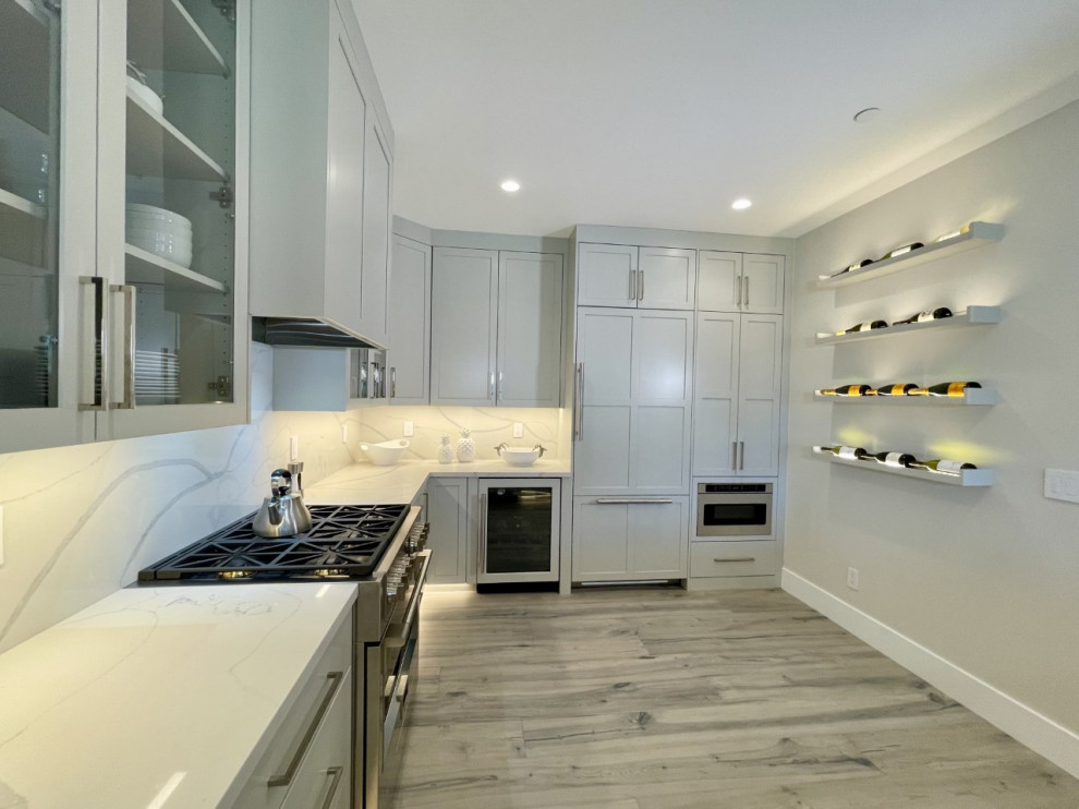 Example of a mid-sized minimalist u-shaped medium tone wood floor and gray floor enclosed kitchen design with a farmhouse sink, shaker cabinets, gray cabinets, quartz countertops, white backsplash, quartz backsplash, paneled appliances, a peninsula and white countertops