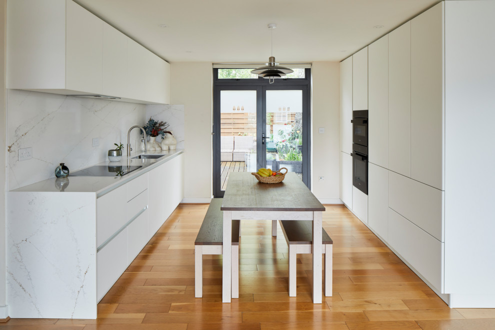 Inspiration for a mid-sized modern single-wall eat-in kitchen in Other with an undermount sink, flat-panel cabinets, white cabinets, quartz benchtops, white splashback, engineered quartz splashback, black appliances, medium hardwood floors, no island, brown floor and white benchtop.
