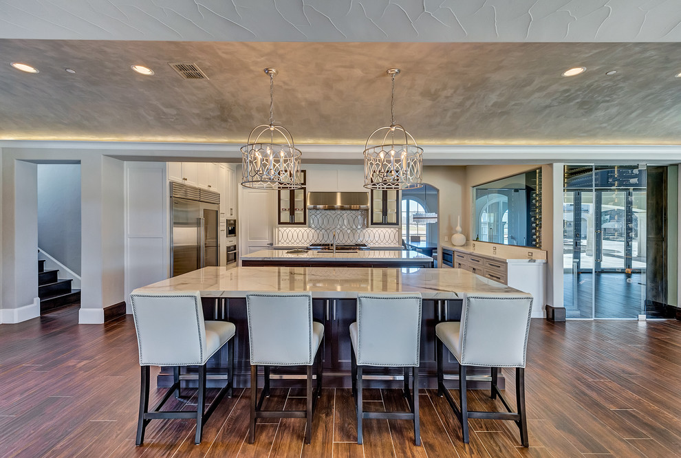 Eat-in kitchen - huge transitional u-shaped ceramic tile and brown floor eat-in kitchen idea in Orange County with an undermount sink, shaker cabinets, white cabinets, marble countertops, white backsplash, marble backsplash, stainless steel appliances and two islands