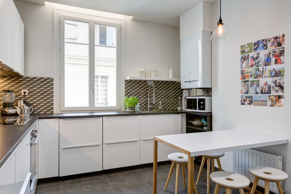 Photo of a mid-sized scandinavian l-shaped separate kitchen in Paris with brown splashback, cement tiles, grey floor, brown benchtop, a drop-in sink, flat-panel cabinets, white cabinets, laminate benchtops, cement tile splashback, black appliances and a peninsula.