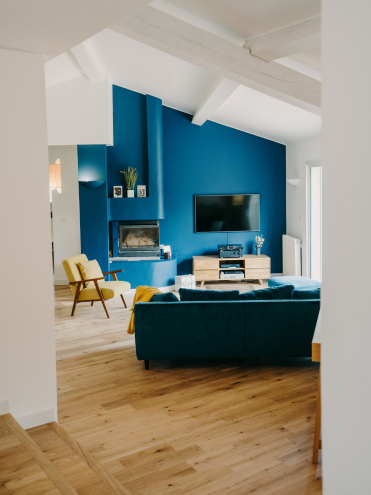 Idées déco pour un grand salon ouvert avec un mur bleu, parquet clair, un poêle à bois, un téléviseur fixé au mur, un sol beige, poutres apparentes et un plafond cathédrale.