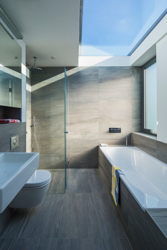 Design ideas for a contemporary bathroom in London with a wall-mount sink, a drop-in tub, a curbless shower, a wall-mount toilet and gray tile.