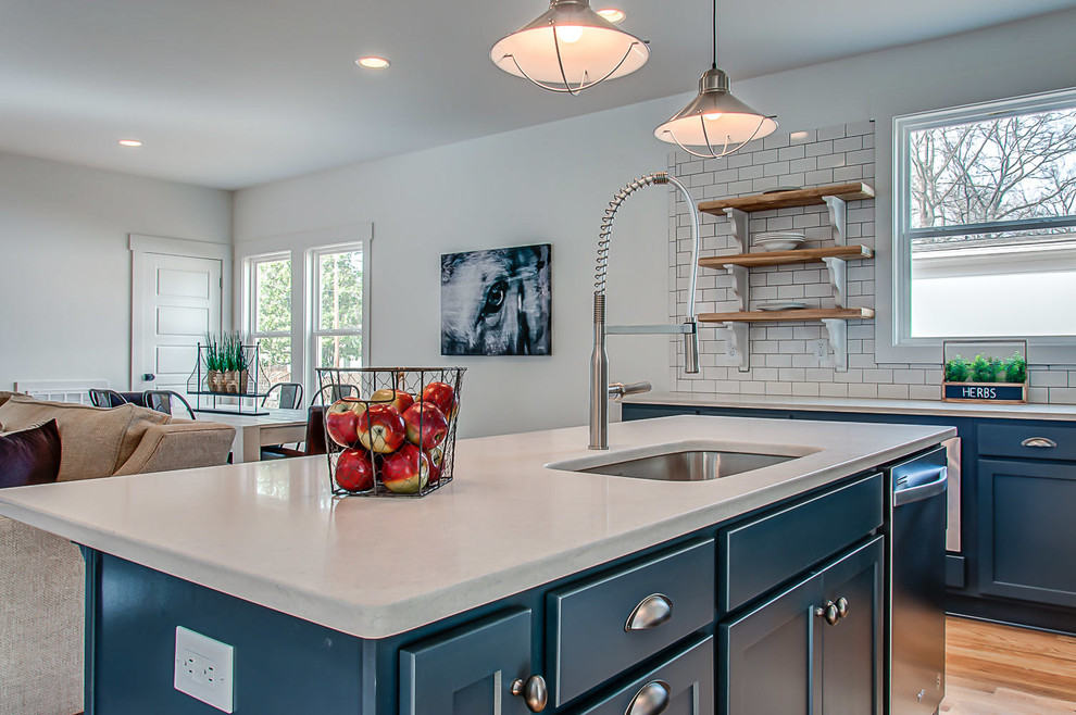 Design ideas for a mid-sized country l-shaped open plan kitchen in Nashville with an undermount sink, shaker cabinets, blue cabinets, quartzite benchtops, white splashback, subway tile splashback, stainless steel appliances, light hardwood floors and with island.
