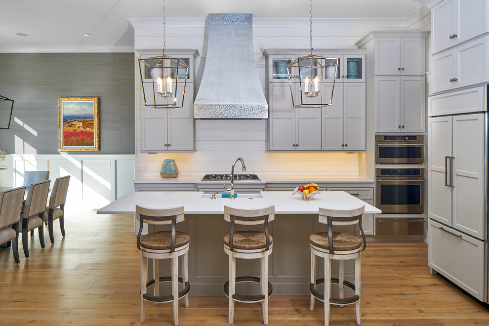 Mid-sized transitional single-wall eat-in kitchen in Charleston with a farmhouse sink, shaker cabinets, grey cabinets, stainless steel appliances, with island, white splashback, timber splashback, light hardwood floors, white benchtop and quartzite benchtops.