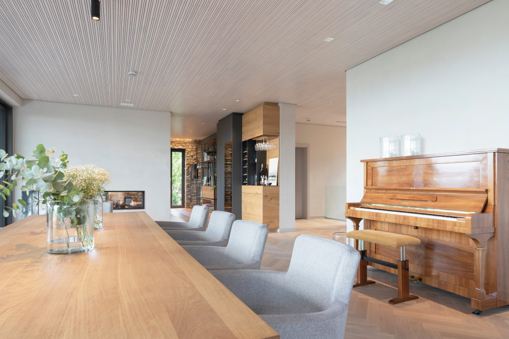 Стильный дизайн: огромная гостиная-столовая в современном стиле с белыми стенами, светлым паркетным полом, двусторонним камином, фасадом камина из металла, бежевым полом и деревянным потолком - последний тренд