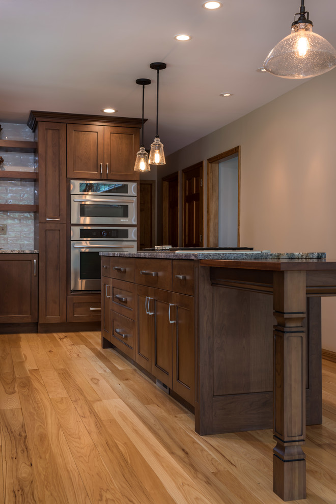 Mid-sized transitional l-shaped eat-in kitchen in New York with a single-bowl sink, recessed-panel cabinets, medium wood cabinets, granite benchtops, white splashback, glass tile splashback, stainless steel appliances, medium hardwood floors and with island.