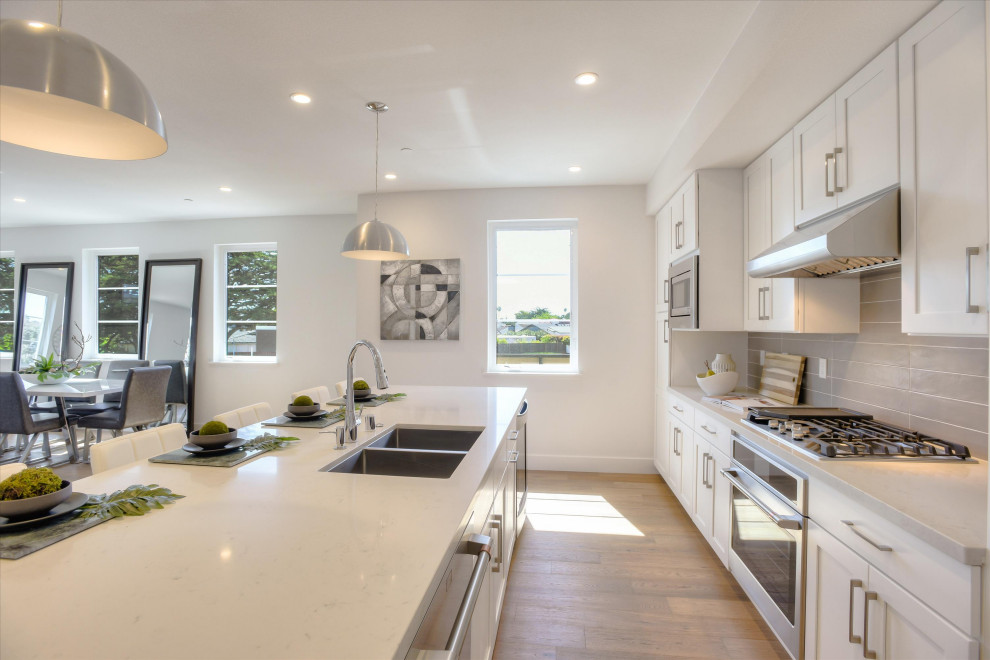 Photo of a contemporary single-wall open plan kitchen in San Francisco with an undermount sink, shaker cabinets, white cabinets, stainless steel appliances, with island and white benchtop.