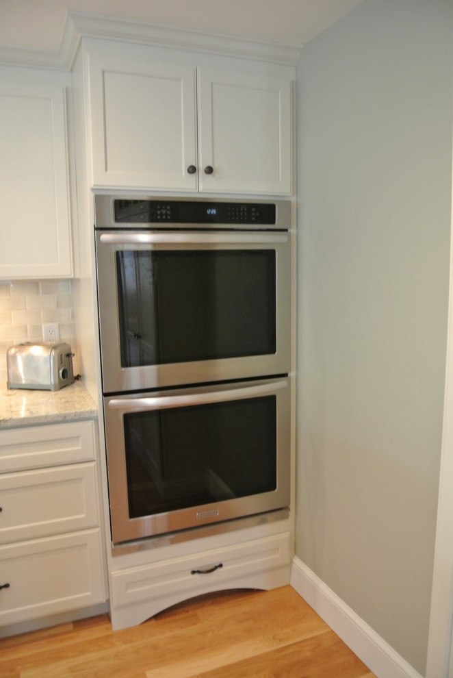 Transitional galley light wood floor eat-in kitchen photo in Boston with an undermount sink, stainless steel appliances, an island, shaker cabinets, white cabinets, wood countertops, white backsplash, ceramic backsplash and brown countertops