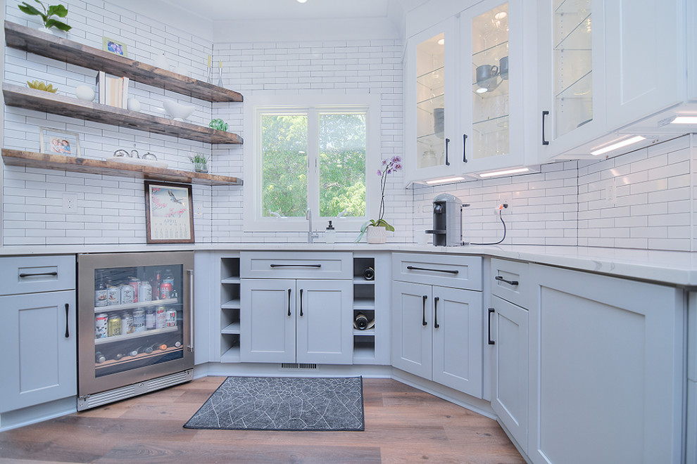 Transitional brown floor kitchen photo in Charlotte with flat-panel cabinets, white cabinets, quartz countertops, white backsplash, ceramic backsplash, stainless steel appliances, an island and white countertops