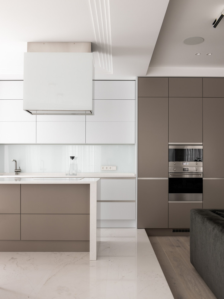 This is an example of a large contemporary galley open plan kitchen in Other with an undermount sink, white cabinets, white splashback, glass sheet splashback, with island, white benchtop, flat-panel cabinets, stainless steel appliances and white floor.