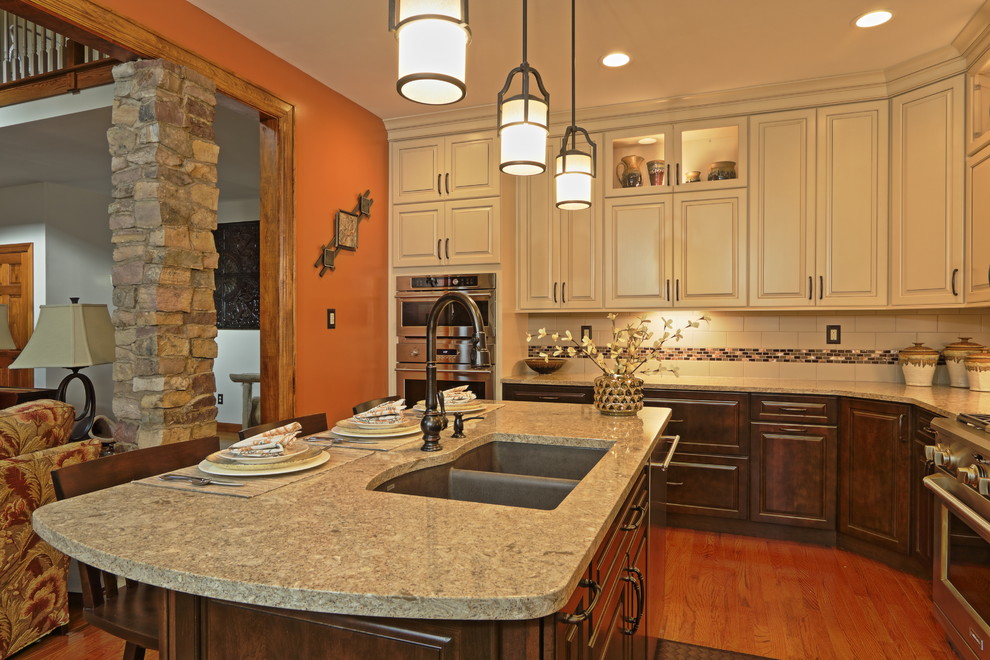 Eat-in kitchen - large transitional l-shaped light wood floor eat-in kitchen idea with an undermount sink, raised-panel cabinets, brown cabinets, quartz countertops, beige backsplash, ceramic backsplash, stainless steel appliances and an island