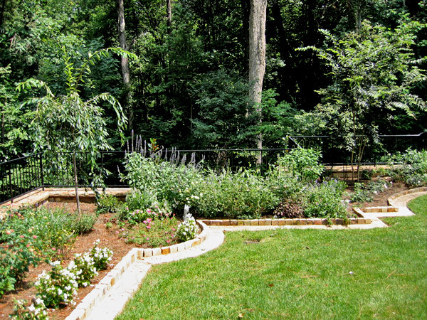 На фото: солнечный регулярный сад среднего размера в классическом стиле с газонным бордюром, хорошей освещенностью, покрытием из каменной брусчатки и с металлическим забором с