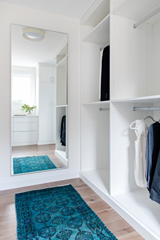 Ejemplo de vestidor actual de tamaño medio con armarios con paneles lisos, puertas de armario blancas y suelo de madera en tonos medios