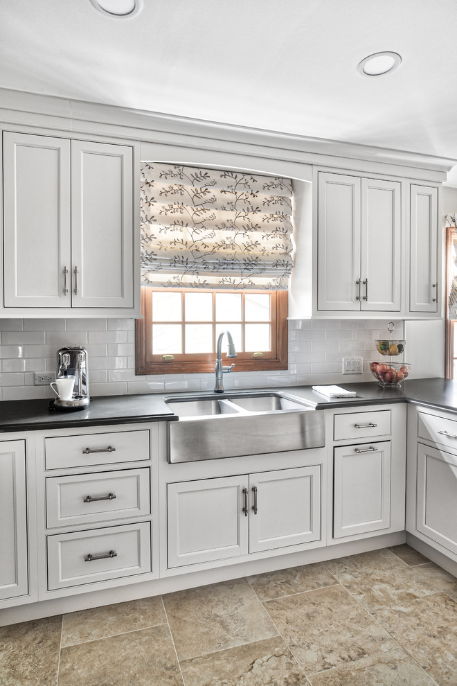 Large transitional u-shaped eat-in kitchen in New York with a farmhouse sink, beaded inset cabinets, white cabinets, white splashback, subway tile splashback, stainless steel appliances, a peninsula and black benchtop.