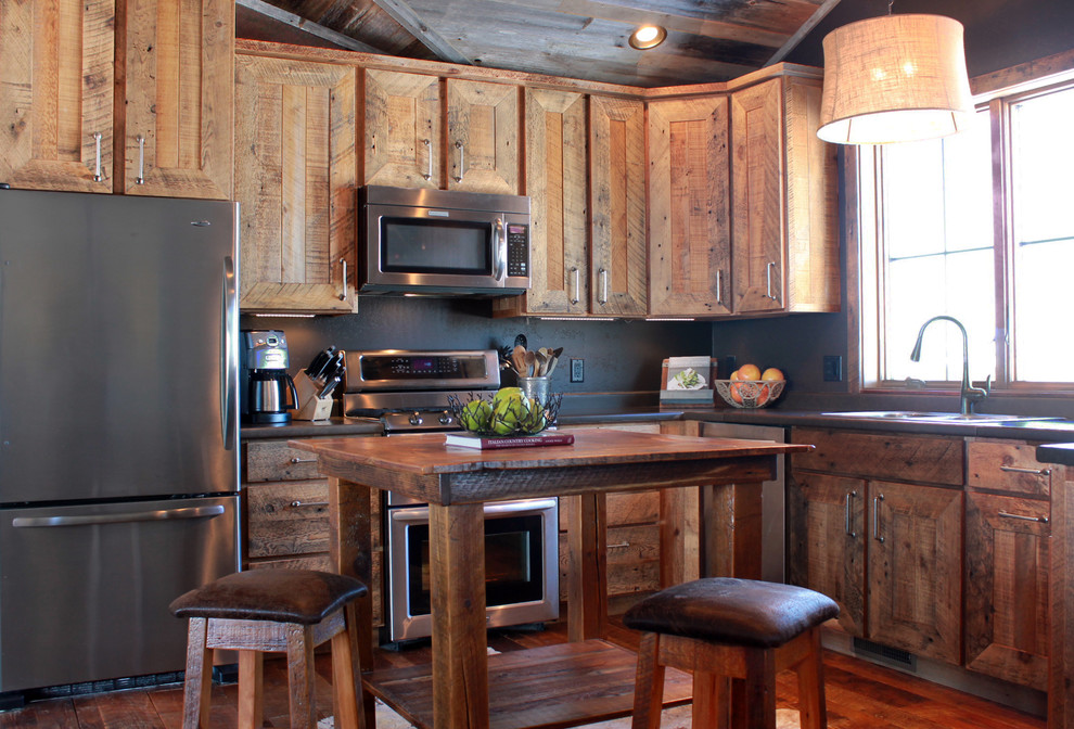 Example of a mid-sized mountain style u-shaped medium tone wood floor eat-in kitchen design with a double-bowl sink, recessed-panel cabinets, distressed cabinets, concrete countertops, stainless steel appliances and an island