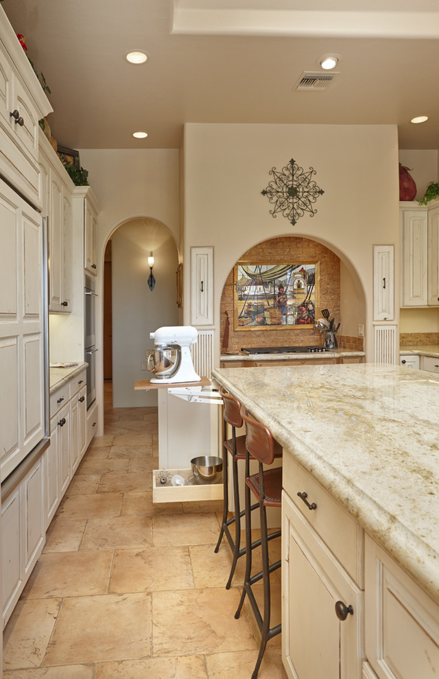Photo of a large country u-shaped eat-in kitchen in Other with a farmhouse sink, raised-panel cabinets, distressed cabinets, granite benchtops, beige splashback, panelled appliances, travertine floors, with island and beige floor.