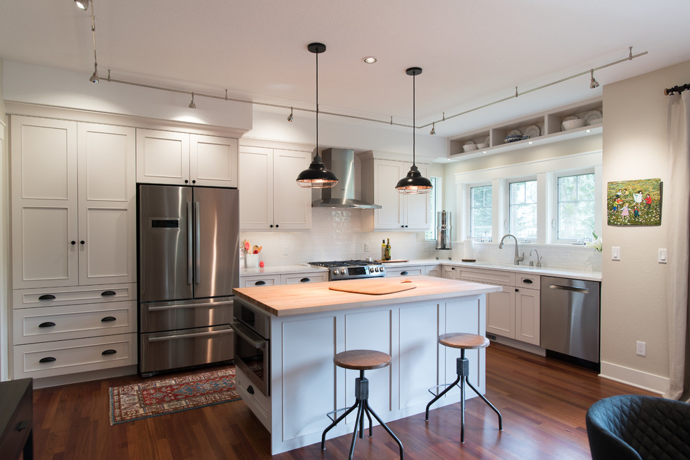 Eat-in kitchen - mid-sized transitional l-shaped medium tone wood floor and brown floor eat-in kitchen idea in Seattle with an undermount sink, recessed-panel cabinets, white cabinets, quartz countertops, white backsplash, ceramic backsplash, stainless steel appliances, an island and white countertops