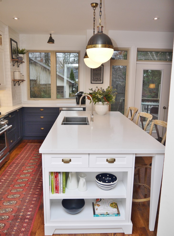 Inspiration for a mid-sized transitional l-shaped medium tone wood floor and brown floor eat-in kitchen remodel in Toronto with an undermount sink, shaker cabinets, blue cabinets, quartz countertops, white backsplash, subway tile backsplash, stainless steel appliances, an island and white countertops