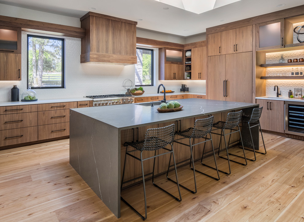 This is an example of a contemporary l-shaped kitchen in Portland with an undermount sink, flat-panel cabinets, medium wood cabinets, medium hardwood floors, with island, brown floor and grey benchtop.