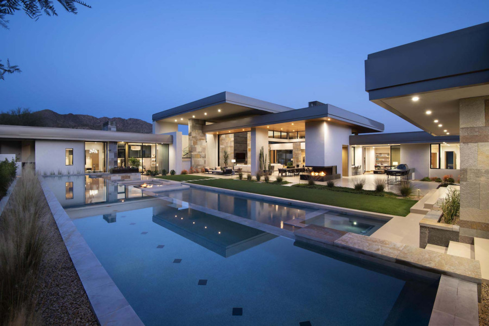 Expansive contemporary two-storey grey house exterior in Phoenix with stone veneer, a flat roof and a grey roof.