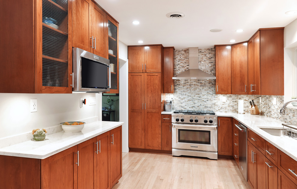 Mid-sized transitional l-shaped separate kitchen in DC Metro with an undermount sink, glass-front cabinets, medium wood cabinets, marble benchtops, multi-coloured splashback, glass tile splashback, stainless steel appliances, light hardwood floors, no island, beige floor and white benchtop.