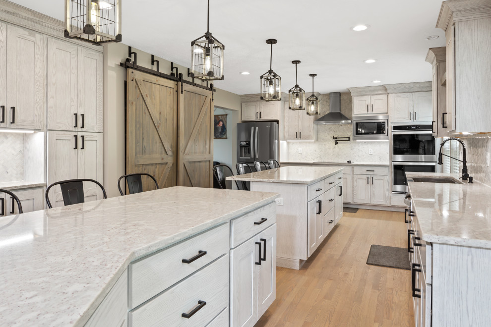 Inspiration for a large country u-shaped eat-in kitchen in Cincinnati with a farmhouse sink, shaker cabinets, white cabinets, granite benchtops, white splashback, marble splashback, stainless steel appliances, light hardwood floors, multiple islands and white benchtop.