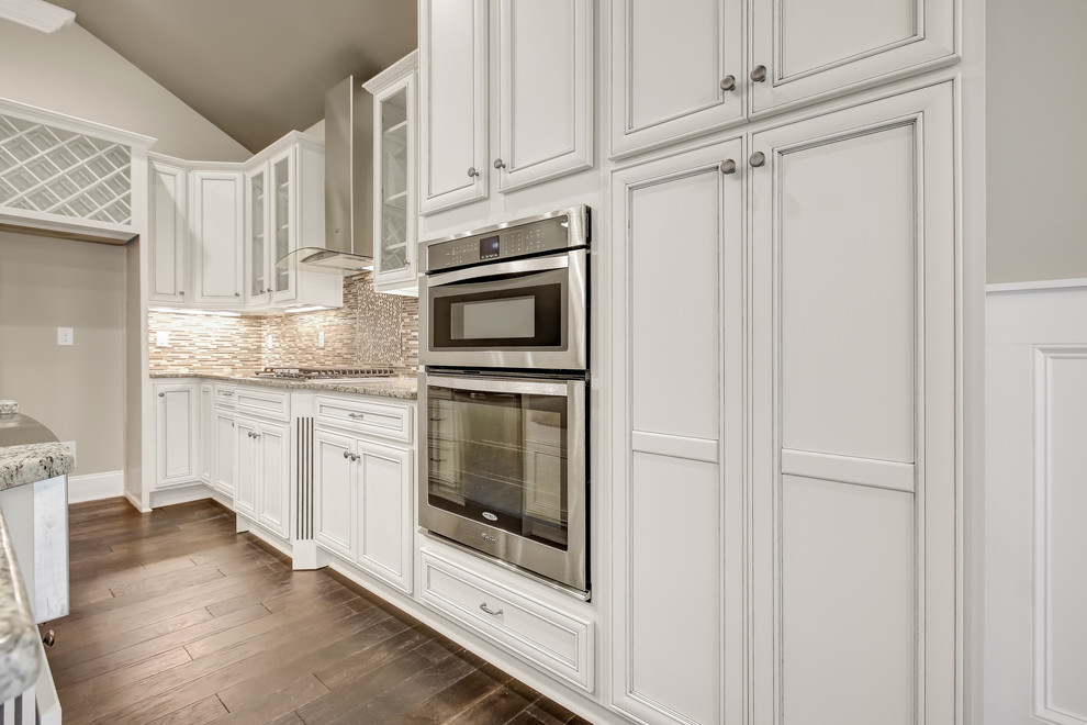 Open concept kitchen - mid-sized transitional l-shaped dark wood floor open concept kitchen idea with a farmhouse sink, recessed-panel cabinets, white cabinets, granite countertops, beige backsplash, mosaic tile backsplash, stainless steel appliances and an island