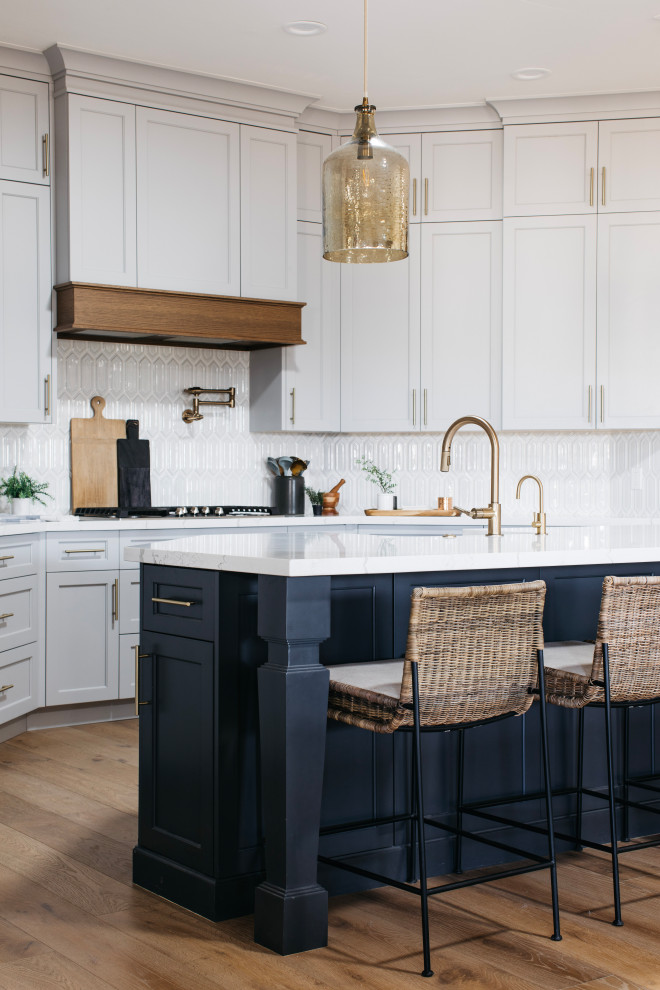 Mid-sized beach style medium tone wood floor and brown floor eat-in kitchen photo in Phoenix with a farmhouse sink, recessed-panel cabinets, blue cabinets, marble countertops, white backsplash, stone tile backsplash, paneled appliances, an island and white countertops