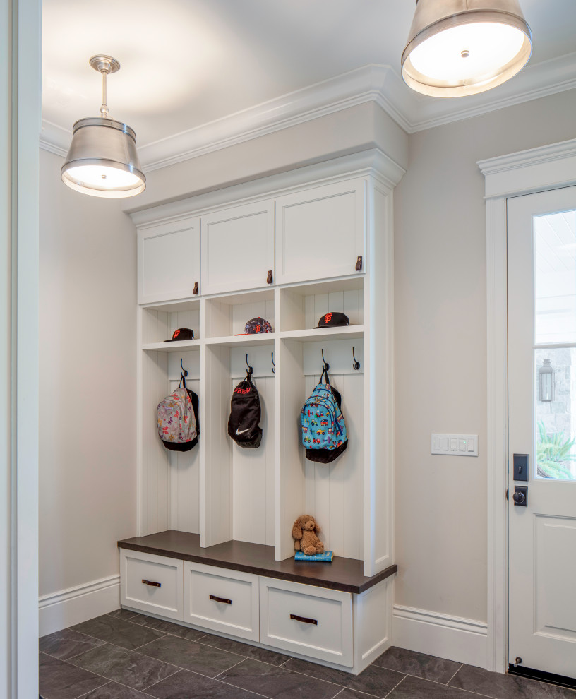 This is an example of a mid-sized beach style galley laundry cupboard in San Francisco with shaker cabinets, white cabinets, wood benchtops, beige walls, slate floors, grey floor and brown benchtop.