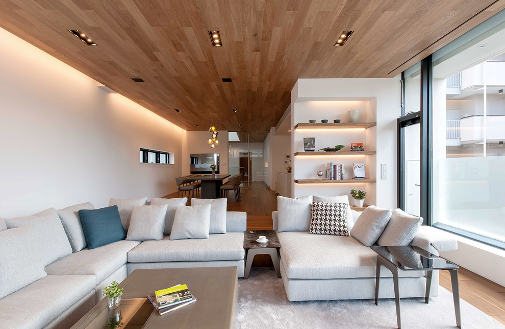 This is an example of a large contemporary formal open concept living room in Tokyo with white walls, medium hardwood floors and a built-in media wall.